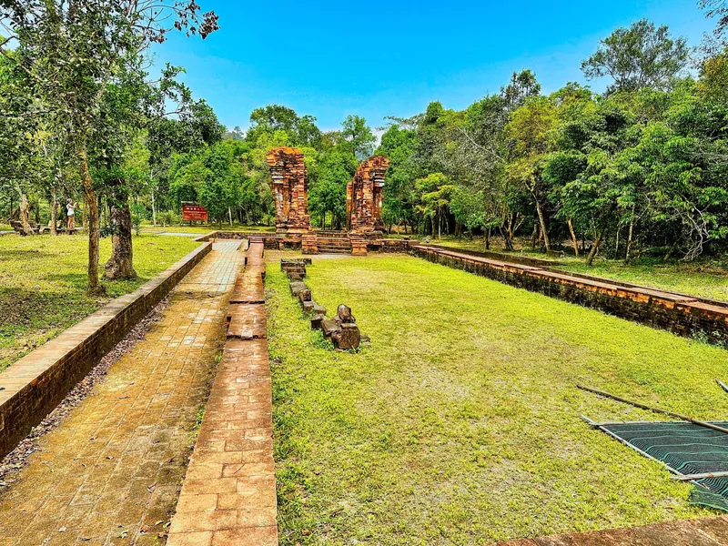 Ancient red brick Cham Hindu temple ruins stand amid green lawns and forest at My Son Sanctuary.