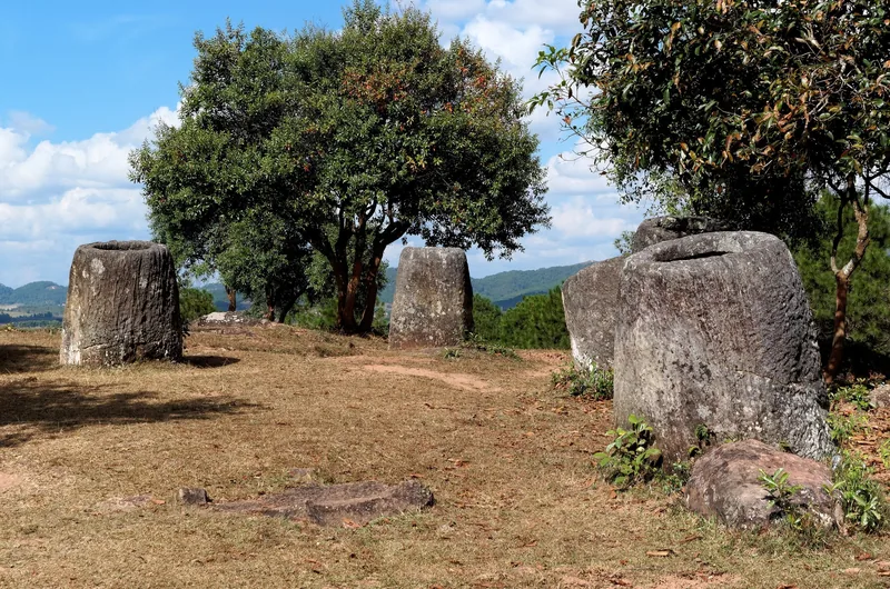 Ancient stone jars scattered across a grassy hillside at the Plain of Jars in Laos.